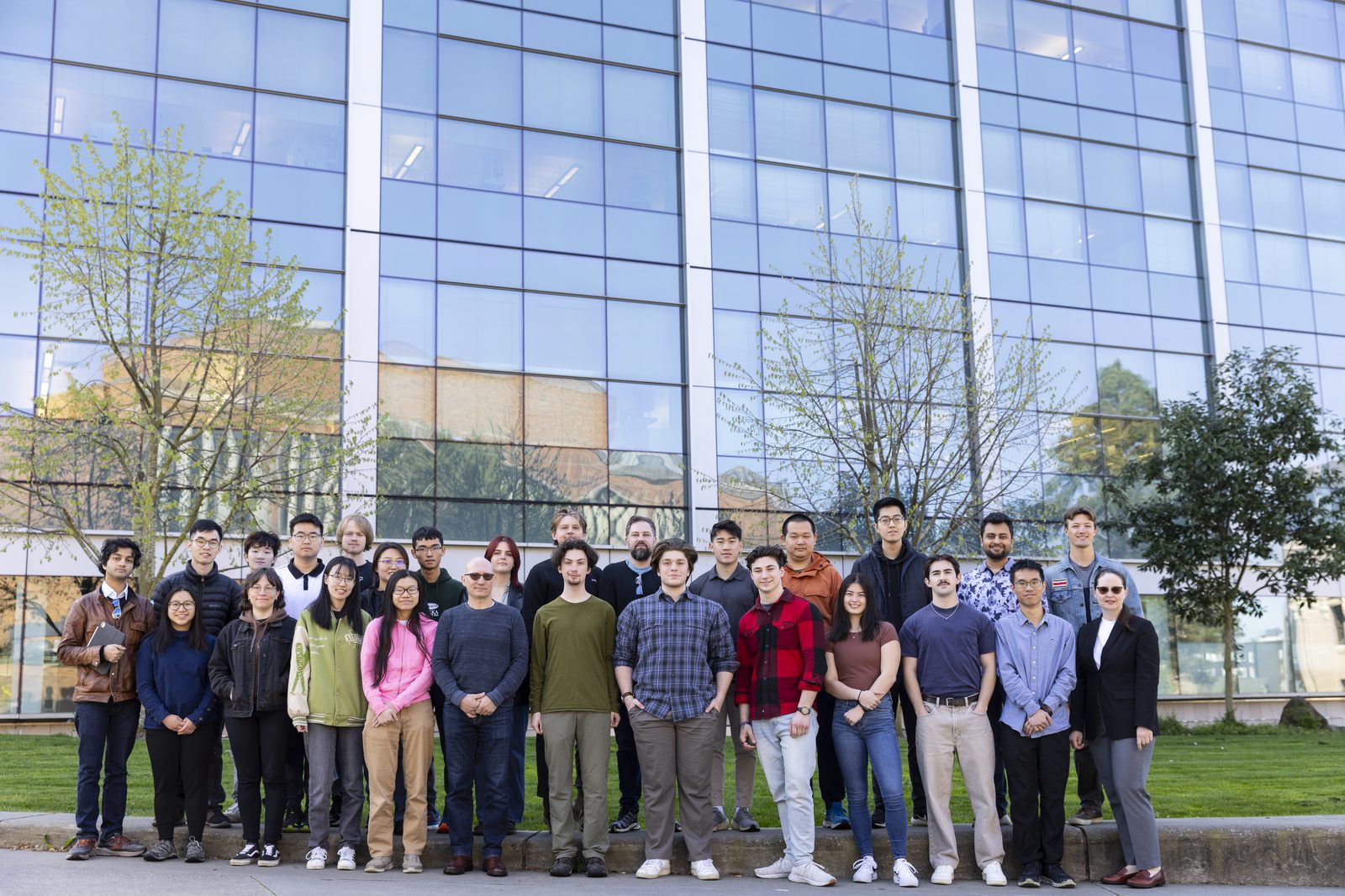 Large group photo of a research group standing outside a glass-fronted research building.