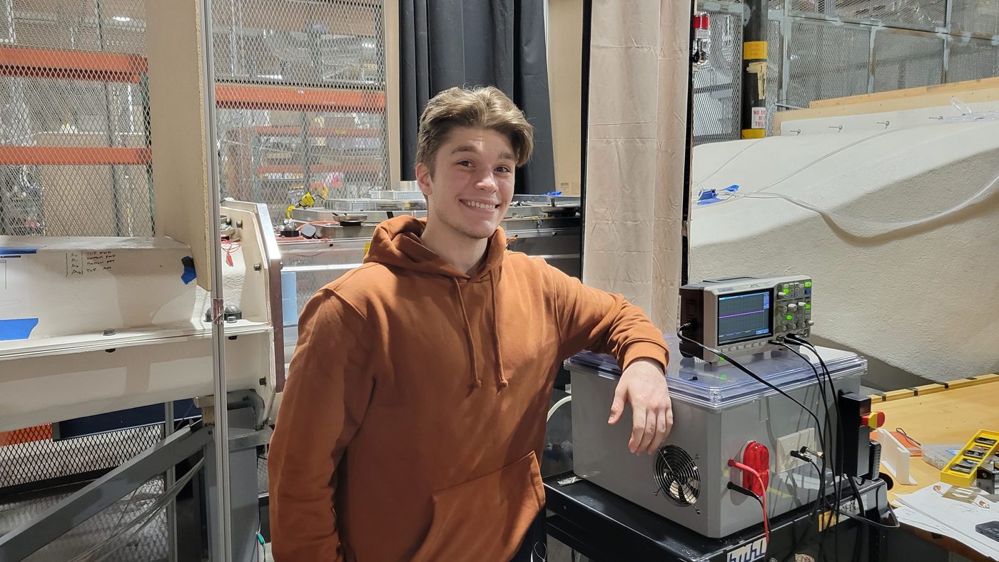 Benjamin Price beside a high-voltage power supply and oscilloscope at the wind-tunnel test section.