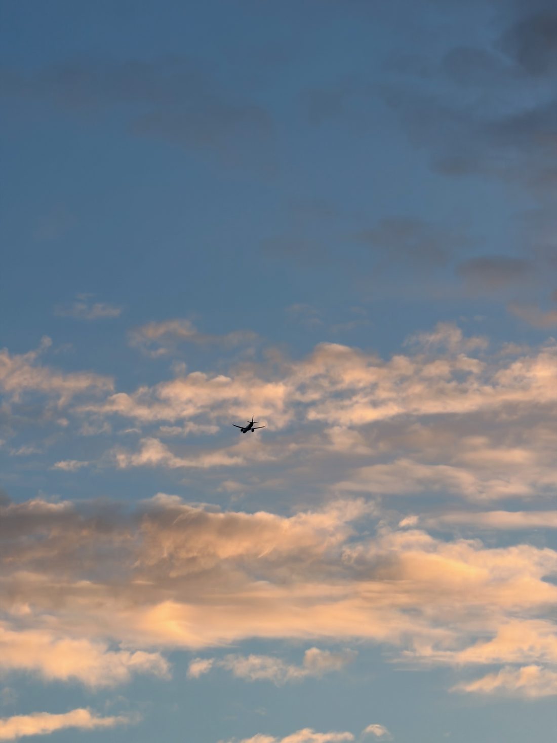 A distant airliner silhouetted against blue and orange sunset clouds.