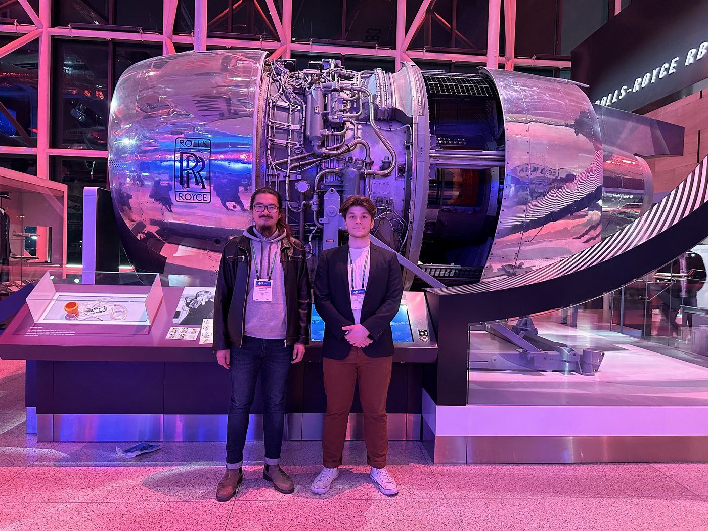 Two people standing in front of a large cutaway Rolls-Royce turbofan engine on museum display.