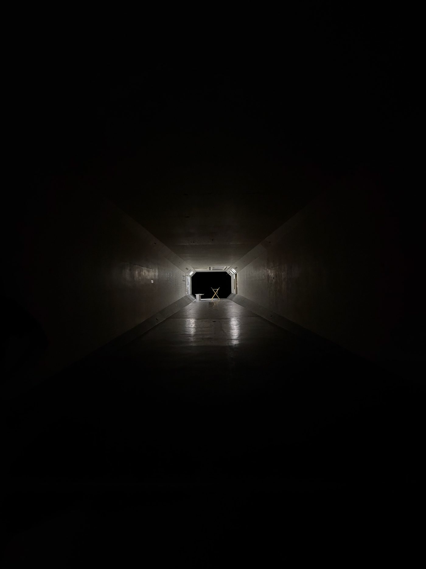 Looking down the long, dark interior of a large wind tunnel toward the distant lit test section.